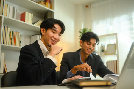 Two businessmen in formal suit reviewing a contract or report together in modern office.の写真素材