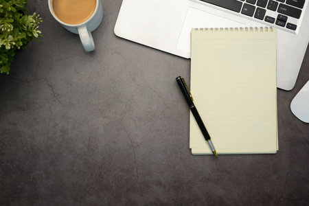Flat lay view of laptop, lined notebook and cup of coffee on a sleek dark stone textured surface.