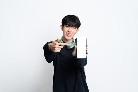 Smiling teenage man holding and pointing at smartphone with black screen for app promotions or tech advertisements.の写真素材