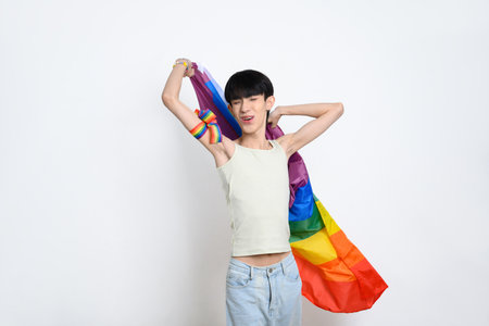 Cheerful young gay man holding a rainbow pride flag on white background. LGBTQ pride and equality concept.の写真素材
