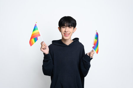 Cheerful man wearing black hoodie holding up rainbow pride flags. Unity and celebration of LGBTQ rights concept.の写真素材