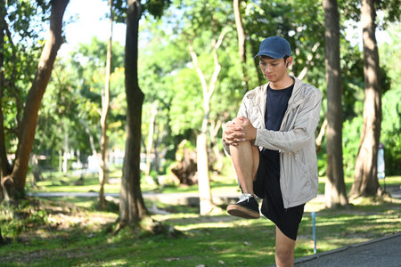 Young sporty man stretching outdoors before running in nature during sunny summer day.
