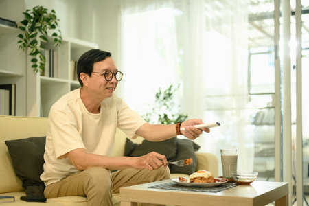 Smiling middle aged enjoying a meal and watching television in living room.の写真素材