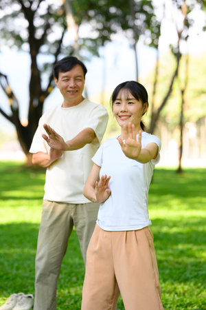 Middle aged father and his adult daughter are enjoying Tai Chi session together in a park.の写真素材