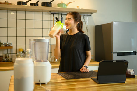 Happy young woman drinking chocolate protein shake in a modern kitchen.の写真素材