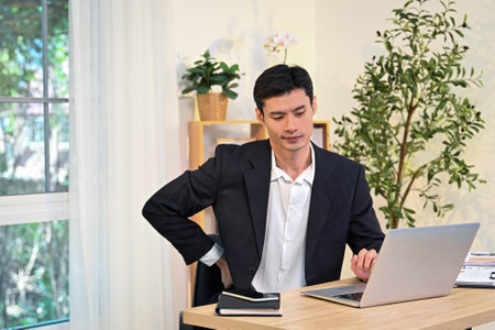 Businessman experiencing back pain from a long sedentary work at the computer in the office.の写真素材