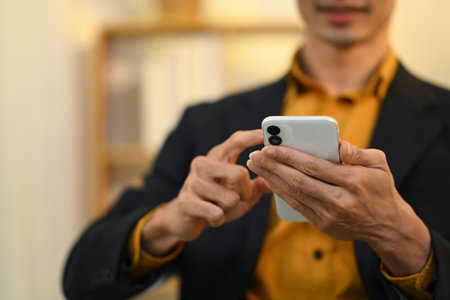 Close up businessman in black suit typing message on his mobile phone.