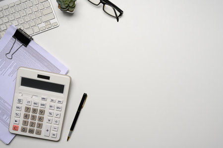 Top view of a tidy workspace with calculator, keyboard, glasses and a stack of documents.の写真素材