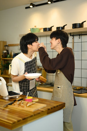 Sweet gay couple feeding each other while preparing a meal in their home kitchen.