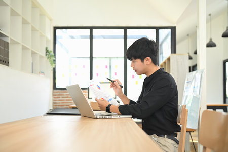 Person reviewing report with charts and graphs while working on a laptop.の写真素材