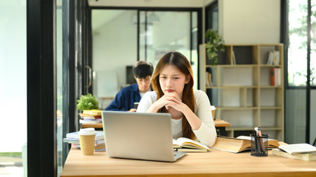 College student concentrating on her laptop in modern study area.の写真素材