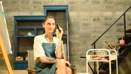 Person in an apron sitting in a studio and talking on mobile phone