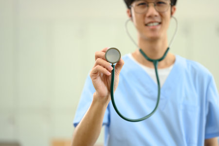 Smiling medical student in scrubs holding a stethoscope towards the camera.の写真素材