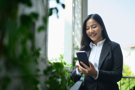 Attractive businesswoman checking her smartphone while standing on office terrace.の写真素材