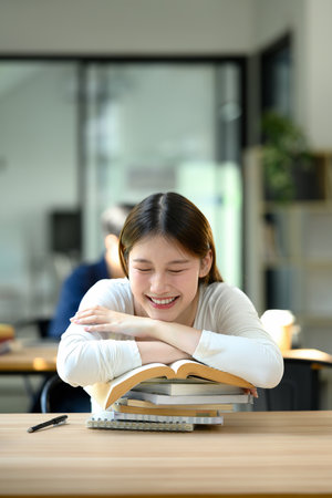Smiling young woman taking a break during study time resting her head on a stack of books.の写真素材