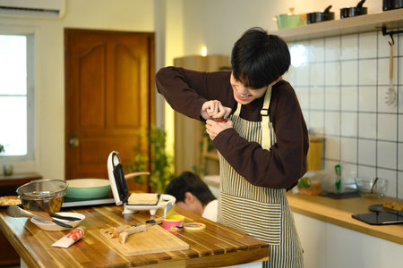 Young man struggles to open a jar while cooking in a cozy kitchen.の写真素材