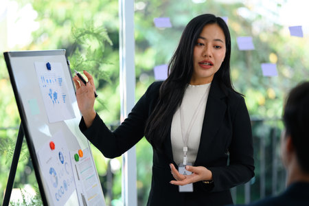 Confident businesswoman in a black suit presenting data on whiteboard during meeting.