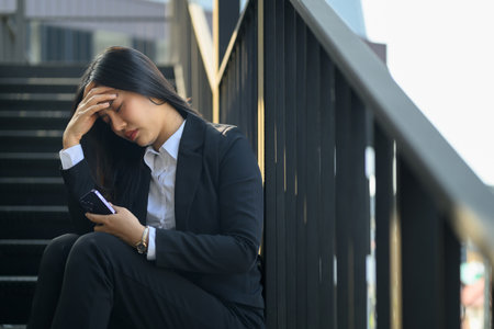 Stressed businesswoman sitting on staircase with her head in her hands in distress.の写真素材