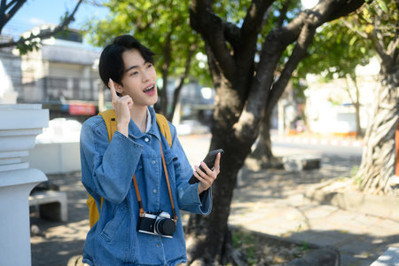 Young traveler with camera around their neck using mobile phone in a sunny urban. Exploration and travel concept.の写真素材