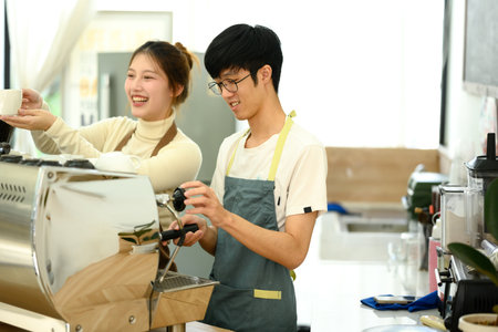 Friendly coffee shop owners wearing aprons working together behind the counter.の写真素材