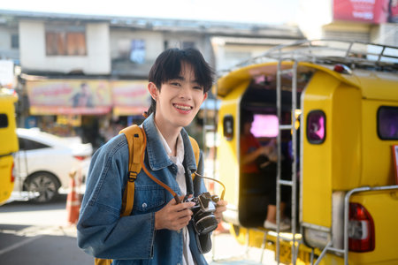 Smiling young traveler with backpack and camera standing in a busy transport station.の写真素材