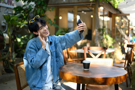 Smiling young asian man with braces waving at the camera while video calling at outdoor cafe.の写真素材