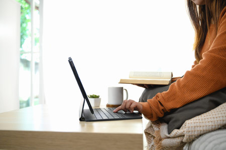 Young woman doing homework while sitting on sofa with book in her hand.