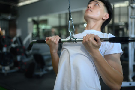 Determined sportsman using a cable machine for a lat pulldown in a gym.