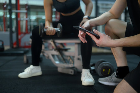 Personal trainer holding digital tablet to assess client performance during a weightlifting...