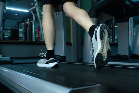 Focused shot of man feet in athletic sneakers running on a treadmill in a modern gym.