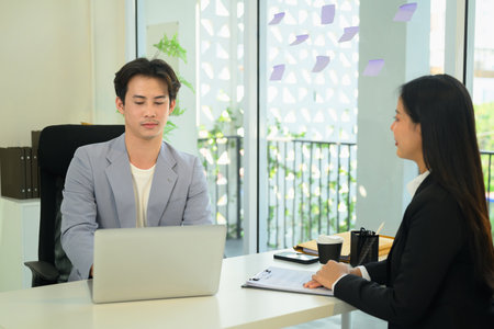 Asian male employe reviewing information on his laptop and evaluates candidate during an interview.の写真素材