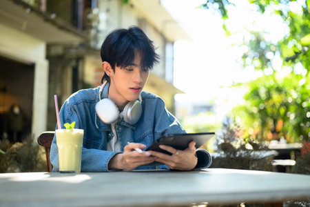 Young stylish man sitting at cafe table with a refreshing beverage and using digital tablet.の写真素材