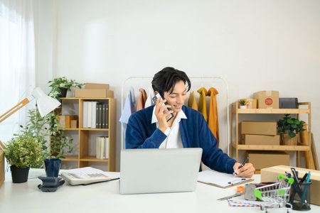 Young entrepreneur running his business from home talking on phone and taking notes.