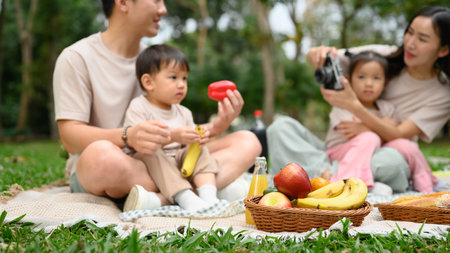Cheerful family enjoys an outdoor picnic on a sunny day. Parenting, outdoor leisure and family bonding concept.の写真素材