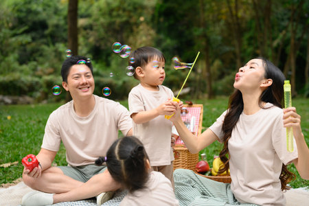 Happy family playing with bubbles and sharing laughter during their picnic in nature.の写真素材