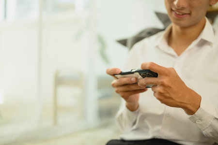 Cropped shot of smiling man enjoying mobile gaming at home.の写真素材
