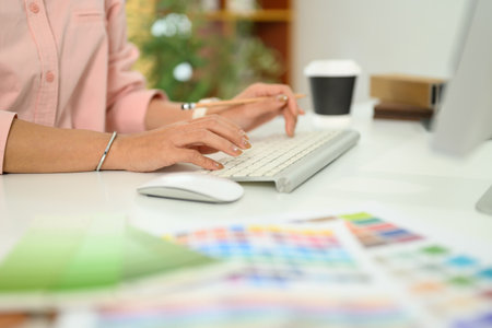 Close up of a designer hands typing on keyboard, surrounded by color swatches and design materials.の写真素材