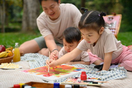 Two little children painting while enjoying a family picnic in the park.の写真素材