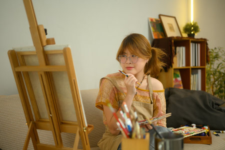 Young artist sitting on couch in studio and contemplating her artwork.の写真素材