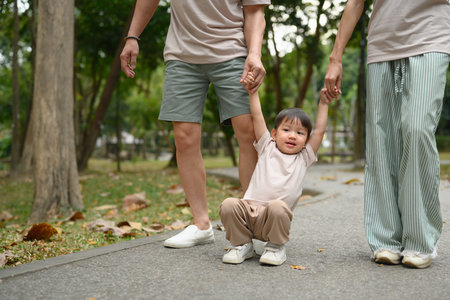 Happy family walking together along a park path, holding hands.の写真素材