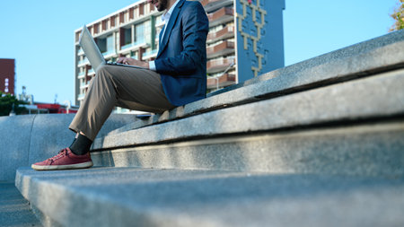Cropped shot of businessman in suit sitting on steps in a city with a laptop.の写真素材