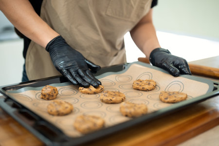 Close up of man placing chocolate chip cookie dough balls on baking tray.