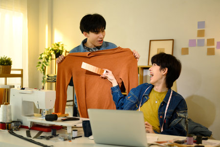 Two young fashion designers comparing fabric colors in a creative studio.の写真素材