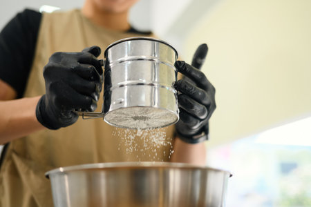 Baker wearing gloves sifting flour for homemade cookies.の写真素材
