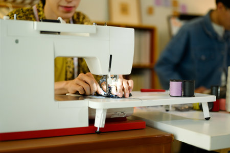Close up of young designer or tailor working on a sewing machine in stylish studio.の写真素材
