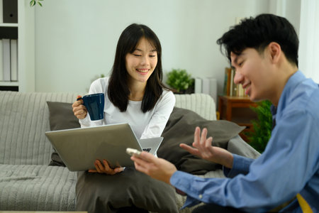 Happy young couple relaxing on a couch using laptop and smartphone.