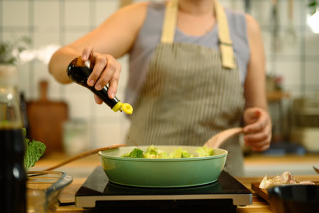 Woman preparing a healthy meal in a kitchen, adding soy sauce into a pan.の写真素材