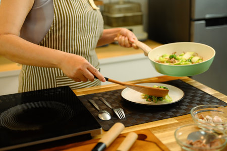 Cropped shot woman serving freshly cooked dish onto a plate in a kitchen.