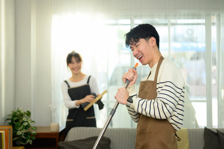 Cheerful young couple having fun while cleaning their home. Daily household chores concept.