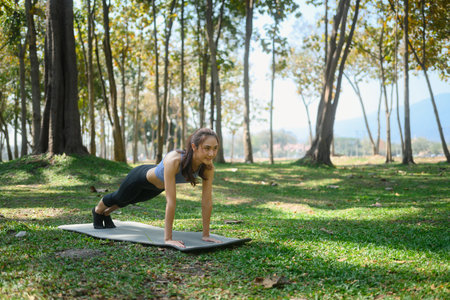 Young woman doing plank exercise on mat in a beautiful green park.の写真素材